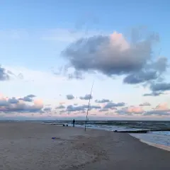 Surfcasting z plaży nad Bałtykiem. Wędkarz przygotowuje zestaw na dalekie rzuty, w tle fale i chmury.