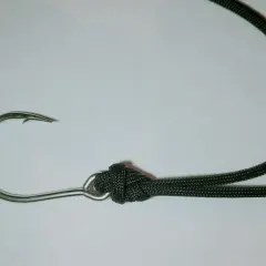 Metalowy haczyk wędkarski z zawiązaną czarną żyłką na łopatce.
