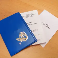 Niebieska okładka karty wędkarskiej z logo ryby i złotym napisem PZW, obok dokumenty.