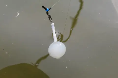 Białe spławiki na rzekę z przepływanką, w kształcie bombki, unoszą się na wodzie, gotowe do połowu.