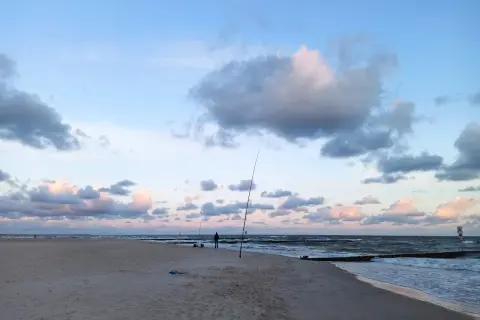 Surfcasting z plaży nad Bałtykiem. Wędkarz przygotowuje zestaw na dalekie rzuty, w tle fale i chmury.