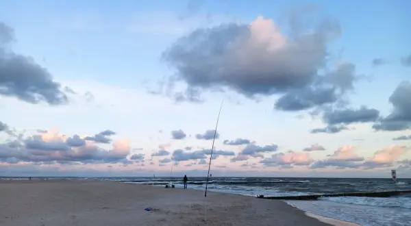 Surfcasting z plaży nad Bałtykiem. Wędkarz przygotowuje zestaw na dalekie rzuty, w tle fale i chmury.
