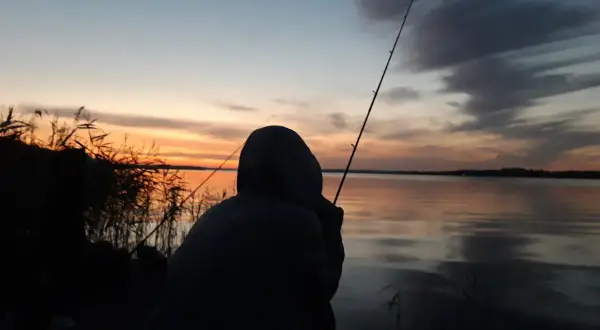Zachód słońca nad jeziorem, wędkarz czeka na branie. Zastanawiasz się, ile kosztuje egzamin i wydanie karty wędkarskiej w starostwie?