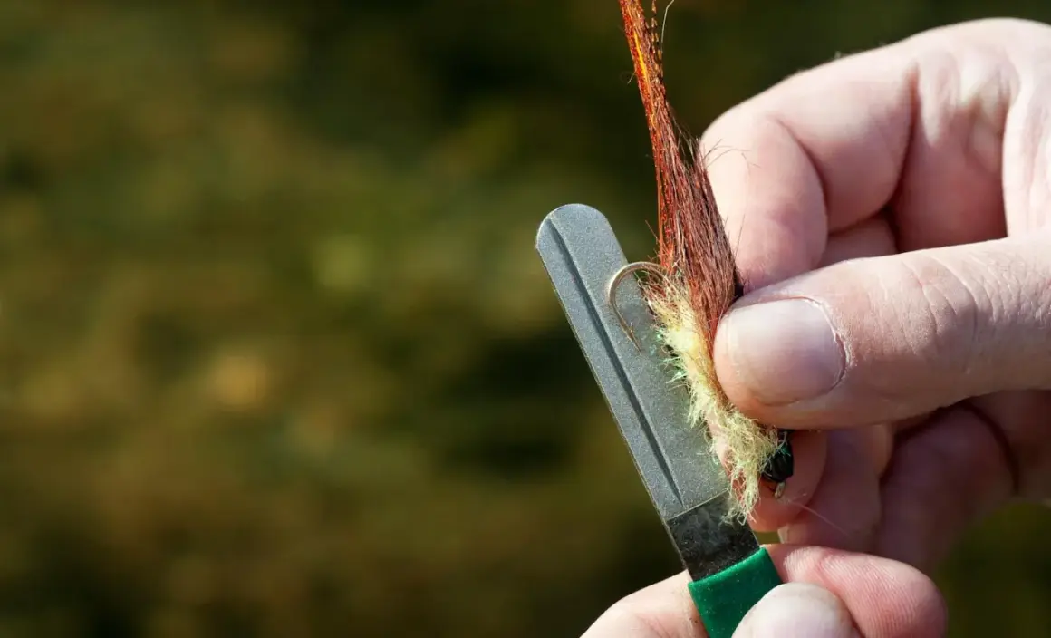 Ręka ostrzy haczyk muchowy na kamieniu, pokazując jak ostrzyć tępe haczyki nad wodą bez specjalnej osełki.
