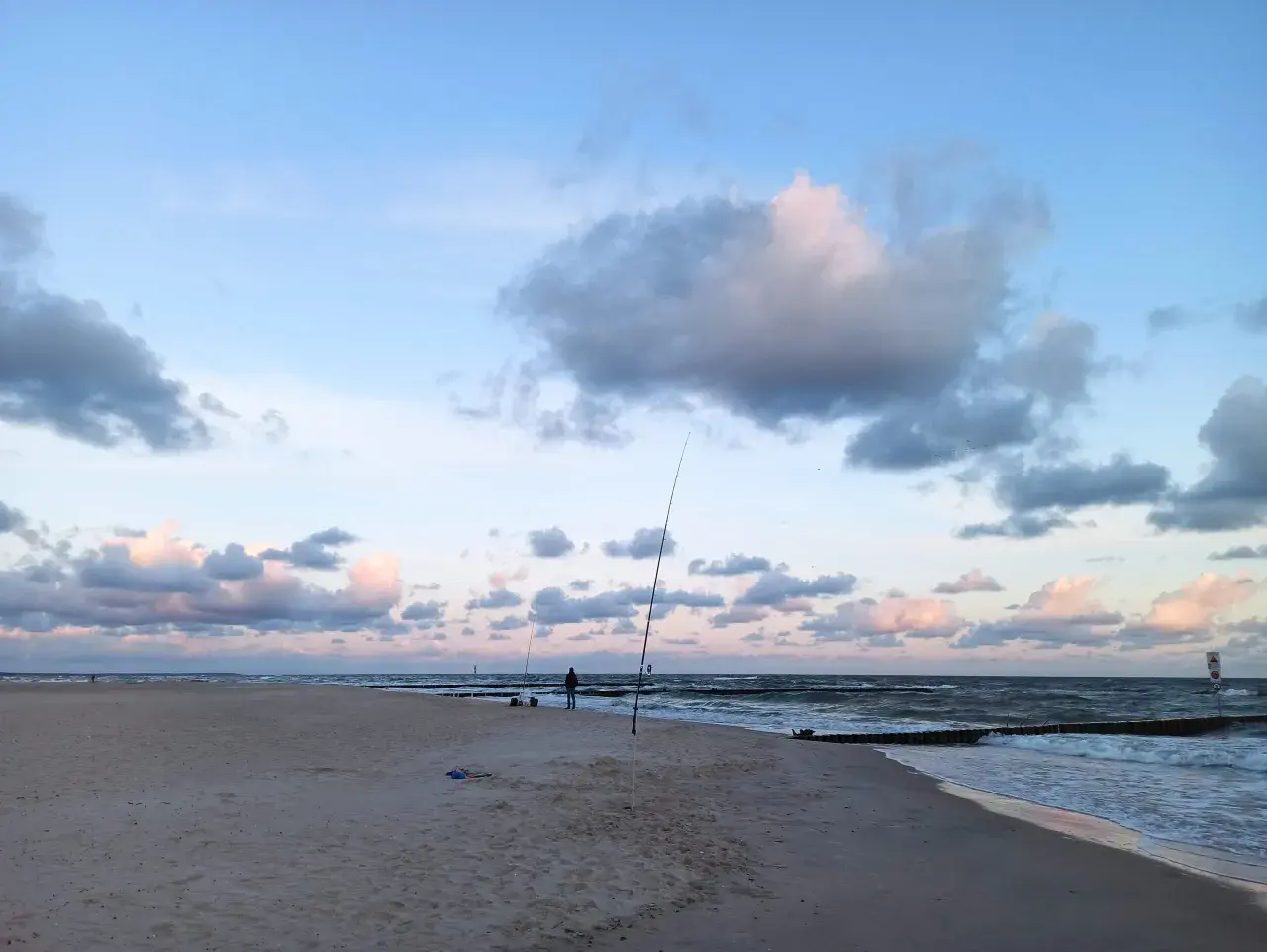 Surfcasting z plaży nad Bałtykiem. Wędkarz przygotowuje zestaw na dalekie rzuty, w tle fale i chmury.