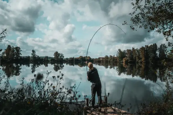 Wędkarz łowi na ciężki spinning z opadu w głębokich rynnach odrzańskich. Wędka wygięta w łuk, woda spokojna, odbija chmury.