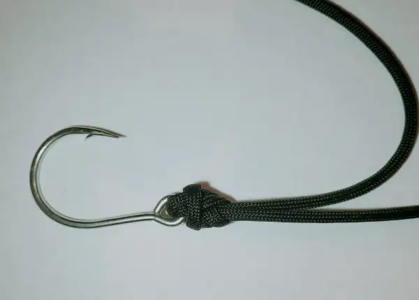 Metalowy haczyk wędkarski z zawiązaną czarną żyłką na łopatce.
